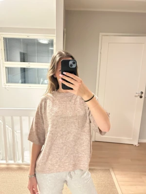 Beige stickad tröja med halvärm - Mysig beige stickad tröja med avslappnad passform och halvärmar. Perfekt för lager-på-lager och chill dagar. Tröjan har en enkel design utan synliga detaljer och är lätt att matcha med olika outfits.