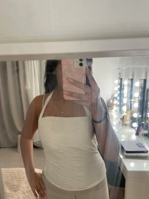 Vit ribbad halterneck linnetopp - Säljer en snygg vit linnetopp med halterneck och ribbad struktur. Toppen har en croppad passform och kan bäras både med och utan band för olika looks. Perfekt till sommaren och enkel att styla med jeans eller kjol.