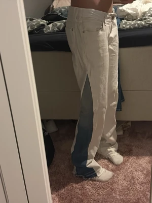 Vita jeans med blå paneler - Unika vita jeans med blå jeanspaneler längs sidorna. Byxorna har normal passform, raka ben och råa kanter vid benslut. Klassisk femficksmodell och midwaist. Snygg kontrast mellan det vita och blå detaljerna, perfekta för dig som vill sticka ut.