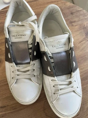 Valentino Garavani vita sneakers - Säljer ett par vita Valentino Garavani sneakers med bred silverfärgad detalj över snörningen. Skorna har klassisk rund tå, vita snören och en chunky sula. Storlek 36 men sitter som 37 (har man 36 normalt sett går det också bra att lägga in en extra sula om man vill)z skriv för fler bilder❤️