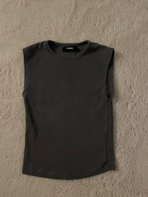 Mörkgrå ärmlös topp från Bikbok - Snygg mörkgrå ärmlös topp från Bik Bok med croppad passform och rund halsringning. Materialet är mjukt och bekvämt, perfekt som basplagg eller för layering under jackor och koftor. Använd bara ett fåtal gånger.