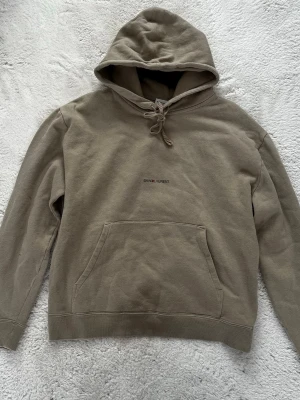 Saint Laurent hoodie - Stilren hoodie från Saint Laurent i en beige/khaki-ton med diskret logotyp på bröstet. Tillverkad i mjuk bomull med bekväm passform och tidlös design.