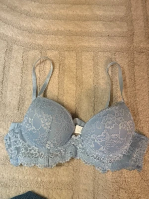 Ljusblå spets-bh  - Söt ljusblå bh från med vadderade kupor och vacker spetsdetalj över hela bh med rosett fram. Storlek 75 A, knappt använd 