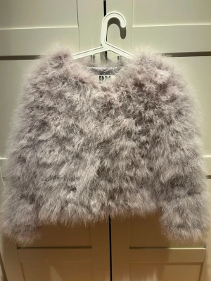 Ljusgrå fluffig pälsjacka - Supersnygg ljusgrå pälsjacka med fluffig look och croppad passform. Jackan har lång ärm och ger en riktigt trendig vibe. Perfekt för dig som vill sticka ut och hålla dig varm med stil.