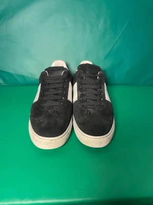 Valentino Garavani svarta sneakers - Snygga sneakers från Valentino Garavani i svart mocka och vitt skinn. Skorna har svarta snören, vita detaljer på sidan och hälen samt coola nitar på sulan. Yttersulan har ett unikt kamouflagemönster. Perfekta för dig som vill ha något extra. Saknas 3 nitar men vi har extra! Men passar också 39,5