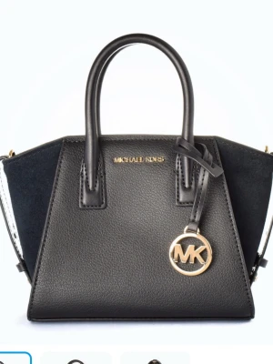 Svart handväska från Michael Kors - Snygg svart handväska från Michael Kors med silverfärgade detaljer och MK-hänge. Väskan har två topphandtag och är tillverkad i skinn med sidor i mocka. Perfekt storlek för det viktigaste och ger en lyxig känsla till din outfit. Nuvarande pris är 3500kr. Skriv för mer bilder.