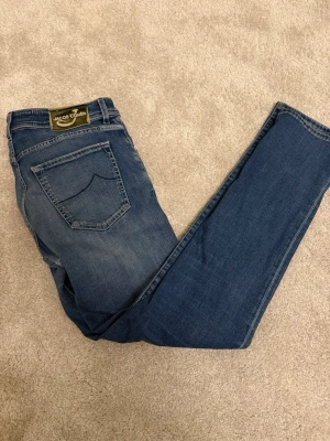 Jacob Cohén Premium Jeans - Storlek 34 - Handgjorda Italienska Jeans - Model 622 - Säljer ett par Exklusiva italienska jeans från Jacob Cohén - ett av världens mest prestigefulla jeansmärken! Det är i underbart skick! Den ända defekten är att märket där bak har krymt lite i tvätten! Handgjorda med italienskt hantverk och premium denim. Ikonisk guldmetallic-knapp med Jacob Cohén-logotyp och vackert mönstrat innerfoder. Dessa jeans kombinerar lyx, kvalitet och perfekt passform på ett sätt få andra märken kan matcha! Detaljer: Märke: Jacob Cohén (Made in Italy) Storlek: 34 