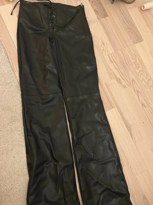 Svarta skinnbyxor från Zara XS - Säljer ett par svarta skinnbyxor från Zara i storlek XS. Byxorna har snörning framtill och dragkedja i sidan för en edgy look. De är raka i modellen och har en snygg, lite glansig finish. Perfekta för dig som vill sticka ut lite extra.