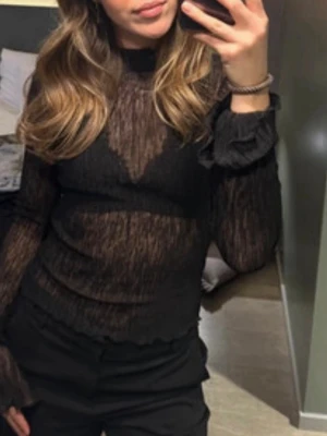 Svart transparent långärmad topp - Säljer en svart transparent långärmad topp med lätt rynkad struktur och volangdetaljer vid ärmslut och nederkant. Toppen är figurnära och har en hög hals, perfekt att styla lager på lager eller med en snygg bralette under.