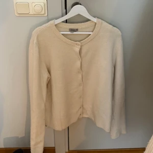 Beige kofta med knappar - Beige kofta med rund halsringning och knäppning framtill. Koftan är nopprig men fullt funktionell därav lägre pris. 