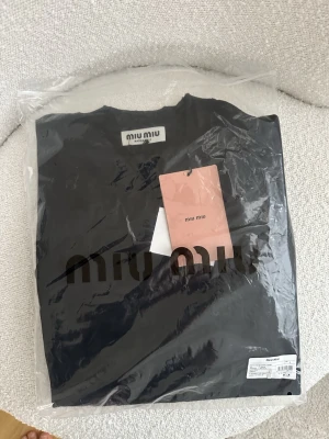 Svart t-shirt från Miu Miu med broderi - Säljer en svart t-shirt från Miu Miu med broderad logga på bröstet och unik broderad design på ryggen. T-shirten har klassisk passform, rund hals och är tillverkad i mjuk bomull. Perfekt för dig som gillar stilrena plagg med exklusiva detaljer.