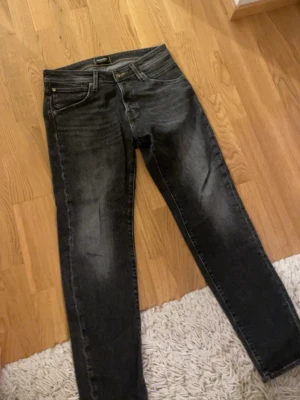 Svarta jeans från Jack & Jones - Säljer ett par svarta jeans från Jack & Jones med snygg tvättad look och klassiska fem fickor. Jeansen har gul kontrastsöm i midjan och smal passform som sitter tajt längs benen. Perfekta till sneakers eller boots.