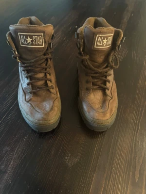 Bruna All Star boots i skinn, strl 43 - Säljer ett par bruna All Star boots i skinn med högt skaft och snörning. Skorna har robust sula och klassisk All Star-logga på plösen. Ovandelen är i läder och insidan är fodrad i textil. Perfekta för dig som vill ha en cool och tidlös look.