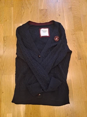 Mörkblå kabelstickad kofta/cardigan Abercrombie - Mörkblå kofta/cardigan från Abercrombie & Fitch i storlek L, men som mer passar för s. Mått: Axelbredd 42 cm/ Längd 66 cm.