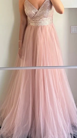 Rosa balklänning med glitter/ paljetter  - Elegant rosa balklänning med glittrig paljettöverdel och omlott-design. Kjolen är i ett luftigt och flödande tyll. Klänningen stängs med snöring där bak och är i storlek 38 men insydd till en 36 (passar en 36 & 38). Endast använd i några timmar och är i nyskick 