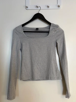 Dam grå långärmad topp  - En stilren grå långärmad med fyrkantig ringning i storlek XS. Toppen är i mjukt och stretchigt material, har en slim passform och är perfekt att matcha med både jeans och kjol. Enkel och clean design som funkar till många olika looks. Använd en gång. 