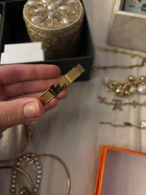 Herme armband guld - Säljer en stilren guldig väst i armbandsmodell med en tydlig H-detalj framtill. Västen är i metall och har en enkel, elegant design som passar till många olika looks. Perfekt accessoar för dig som gillar minimalistiska smycken med en twist.