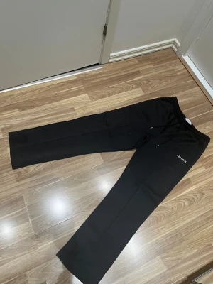 Svarta byxor från Les Deux - Säljer ett par svarta byxor från Les Deux med rak passform och diskret snörning i midjan. Byxorna har minimalistisk design och är tillverkade i ett mjukt material som känns skönt mot huden. Perfekta för en clean och stilren look.