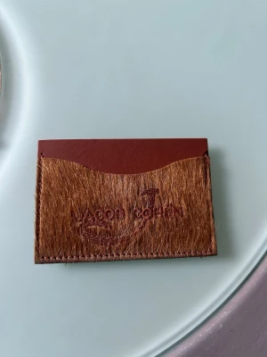Brun plånbok från Jacob Cohën - Säljer en unik plånbok från Jacob Cohën i brunt skinn med pälsdetalj på framsidan. Plånboken har ett stilrent och kompakt format, perfekt för kort. Loggan är snyggt broderad på framsidan.