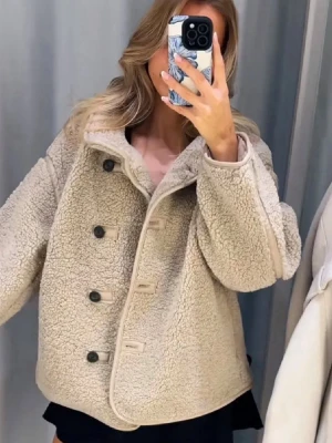 Beige teddyjacka med knappar - Säljer en supermjuk och fluffig beige teddyjacka med stora svarta knappar framtill. Jackan har en oversized passform och hög krage som ger extra mysfaktor. Perfekt för dig som vill ha en varm och trendig look under kyliga dagar.