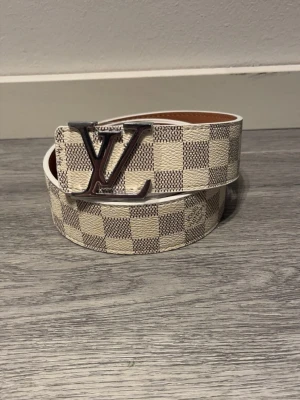 L-bälte  - Snyggt L-bälte i Damier-mönster med silver spänne. Storlek: 110 cm