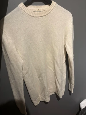 Vit stickad tröja från John Henric - Klassisk vit stickad tröja från John Henric i storlek S. Tröjan har rund halsringning med ribbade muddar vid hals, ärmslut och nederkant. Enkel och stilren design som passar perfekt till lager på lager under höst och vinter. 