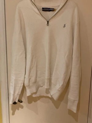 Vit half zip från Polo Ralph Lauren - Säljer en clean vit långärmad tröja från Polo Ralph Lauren med half zip och diskret logga på bröstet. Tröjan är i bomull och har en klassisk passform med ribbade muddar. Perfekt till jeans för en stilren look.