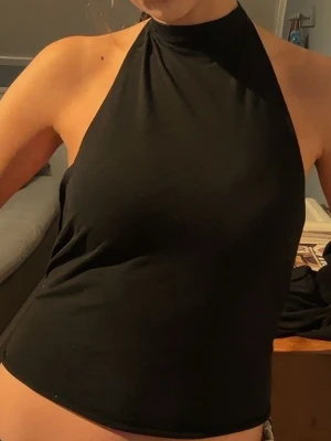 Svart halterneck linnetopp - Säljer en svart halterneck linnetopp med knyt i nacken och ryggen. Toppen är ärmlös och har öppen rygg, vilket ger en snygg och trendig look. Perfekt att matcha med jeans eller kjol för en cool outfit.