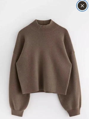 Brun stickad tröja med hög hals - Säljer en brun stickad tröja med hög hals och ballongärmar. Tröjan har en loose passform och ribbade muddar vid hals, ärmslut och nederkant. Perfekt för lager på lager under kyliga dagar.