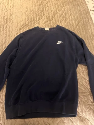 Mörkblå sweatshirt från Nike - Klassisk mörkblå sweatshirt från Nike med vit logga broderad på bröstet. Tröjan har rund halsringning och långa ärmar. Perfekt för en avslappnad och sportig stil. Tillverkad i mjuk bomullsmix för extra komfort.