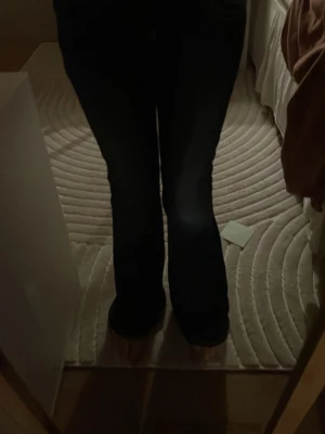 Mörk blåa bootcut jeans med kontrastsömmar - Säljer ett par mörk blåa jeans med bootcut-modell och vita kontrastsömmar. Jeansen har en klassisk femficksdesign och är tillverkade i ett stretchigt jeansmaterial som sitter snyggt över höfterna och låren innan de släpper ut vid bensluten.