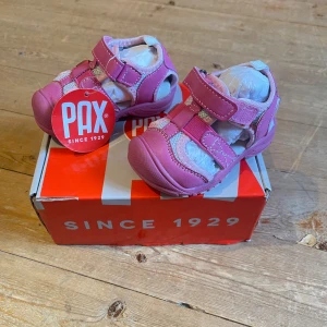 Skor från PAX strl 20 - Helt oanvända pax skor med kartongen. Snygga rosa sandaler från PAX med praktisk kardborreknäppning och ventilerande meshpartier. Skorna har en rund tå, platt sula med vit och rosa mönstrad undersida. Perfekta skor.