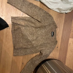 Ljusbrun stickad tröja från Pieces - Säljer en snygg ljusbrun stickad tröja från Pieces. Tröjan har  ett diskret mönster i stickningen. Den har långa ärmar och ribbade muddar vid ärmslut och nederkant. Perfekt för dig som vill sticka ut lite extra!