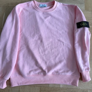  Stone Island sweatshirt - Säljer en ljusrosa sweatshirt från Stone Island med klassisk logga på ärmen. Tröjan har rund halsringning, ribbade muddar och är tillverkad i mjuk bomull. Perfekt för dig som gillar streetwear och vill sticka ut med en snygg färg.