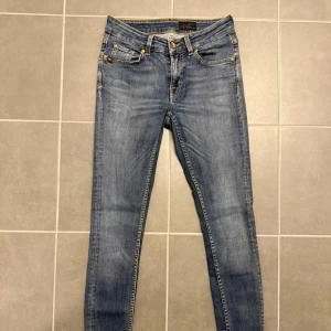 Tiger of Sweden blå jeans - Snygga blå jeans från Tiger of Sweden med skinny passform och klassisk femficksdesign. Jeansen har gul kontrastsöm, läderpatch med logga bak och metallknapp framtill. Perfekta för dig som gillar stilrena och smala jeans. Storlek 28/30