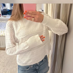 Vit spetsstickad långärmad tröja - Säljer en vit långärmad tröja med snyggt spetsstickat mönster och ribbade muddar. Tröjan har en relaxed passform och är perfekt att matcha med jeans för en fräsch look. Materialet känns mjukt och luftigt, vilket gör den skön att bära.