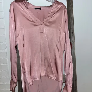 Ljusrosa sidenblus från Stockh LM - Säljer en elegant ljusrosa blus från Stockh LM i mjukt sidenmaterial. Blusen har v-ringad hals, långa ärmar med breda manschetter och en lätt glansig finish. Perfekt för dig som gillar en feminin och stilren look.