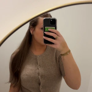 Beige stickad kofta med knappar  - Superfin beige stickad kofta i storlek XS med rund hals och korta ärmar. Koftan har snygga knappar framtill och en mjuk, skön känsla. Perfekt att styla med jeans eller kjol för en chill look.