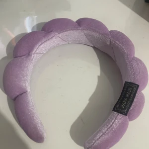 Lila vadderat diadem i sammet - Superfint lila diadem i sammet med vadderad, bubblig design som ger en trendig och lekfull look. Perfekt accessoar för att lyfta din outfit med en pop av färg och mjuk känsla. Märkt med 'Hand Made' på insidan.