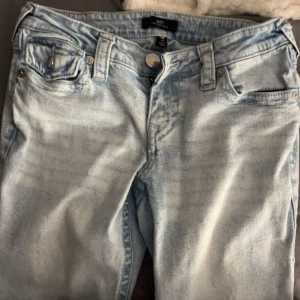 True Religion ljusblå jeans med broderi - Säljer ett par ljusblå jeans från True Religion med snyggt broderade bakfickor och silverfärgade knappar. Jeansen har klassisk femficksdesign, raka ben och cool tvättad look. Perfekt för dig som gillar streetstyle och detaljer.