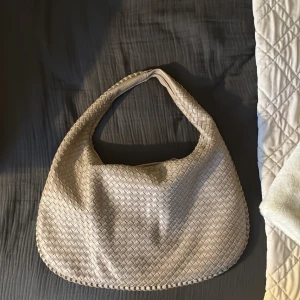 Beige väska från design by si - Beige flätad väska från design by si. Använd ett fåtal gånger och som nyskick. Rymning med ett stort fack inuti och två mindre på sidorna