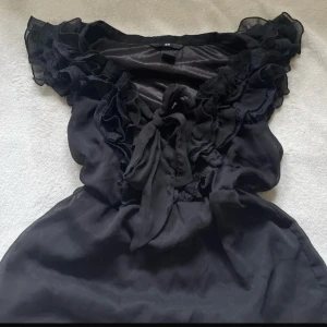 Svart volangblus  - Supersöt svart volangblus från H&M med volanger längs axlar och urringning. Storlek 38 