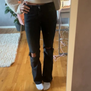 Svarta bootcut jeans med hål på knäna - Säljer ett par svarta jeans med bootcut-modell och hål på båda knäna. Jeansen har klassisk femficksdesign och normal passform. Jeansen är från Nelly och är i storleken xs😘