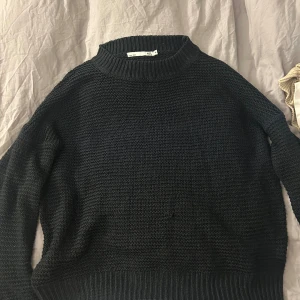 Svart stickad tröja från lager 157 - Svart stickad tröja från lager 157 med grovstickad struktur och ribbad hals, ärmslut och nederkant. Tröjan har en klassisk rund hals och långärmade ärmar, perfekt för dig som gillar enkel och stilren design.