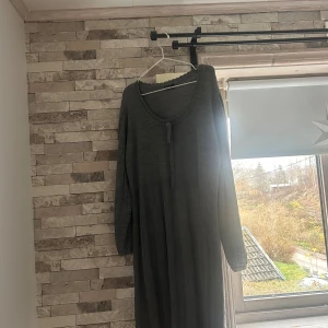 Grå lång stickad klänning Bodyflirt - Mysig grå långklänning från Bodyflirt i stickad material. Klänningen har rund halsringning med dekorativ knappdetalj framtill och långa ärmar. Perfekt för dig som gillar en loose och avslappnad passform.