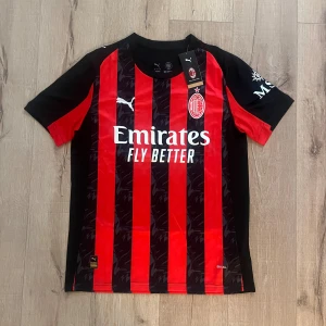 AC Milan kortärmad matchtröja Puma S - AC Milan fotbollströja från Puma i storlek S. Tröjan har klassiska röda och svarta vertikala ränder, klubbmärke på bröstet och sponsortryck. Materialet är lätt polyester med rund hals och korta ärmar. Perfekt för dig som vill representera Milan på träning eller match.