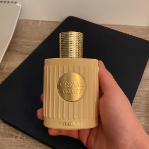 Cream Velvet parfymflaska - Snygg parfym från Khadlaj med modern design och guldiga detaljer. Perfekt för dig som vill sticka ut med din stil. Flaskan har en lyxig känsla och passar bra i väskan eller på hyllan.