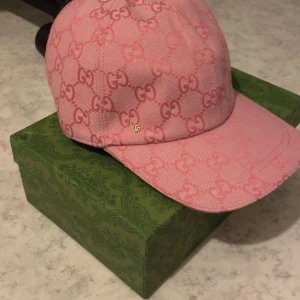 Rosa Gucci keps med GG-mönster - Säljer en rosa keps från Gucci med ikoniskt GG-mönster över hela kepsen. Kepsen har justerbart spänne i rosa läder och är tillverkad i bomullscanvas. Perfekt accessoar för dig som vill sticka ut med lyxig streetstyle.