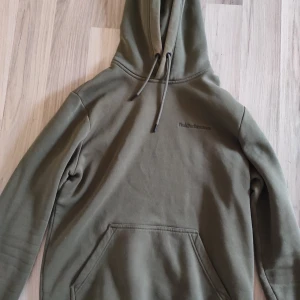 Olivgrön hoodie från Peak Performance - Säljer en olivgrön hoodie från Peak Performance med diskret logga på bröstet. Tröjan har huva med snörning, stor magficka och ribbade muddar vid ärmslut och nederkant. Perfekt för chill dagar och streetwear-stil.