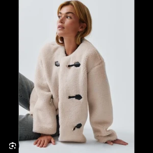 Beige teddyjacka från Gina Tricot - Säljer en beige teddyjacka från Gina Tricot i storlek M. Jackan har rund hals, långärmade ärmar och coola svarta spänndetaljer framtill. Materialet är mjukt och fluffigt, perfekt för att hålla dig varm under höst och vinter. Passformen är loose och riktigt chill.
